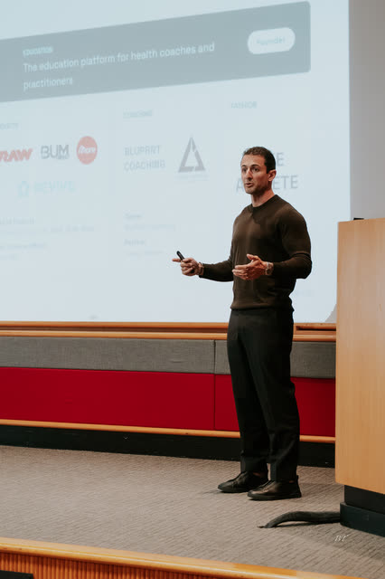 Speaker in a dark sweater mid-talk on stage, clicker in hand