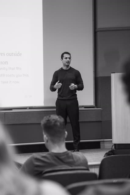 Black and white shot of a speaker talking with both hands, audience in the foreground