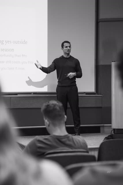 Black and white shot of a speaker gesturing toward his slide