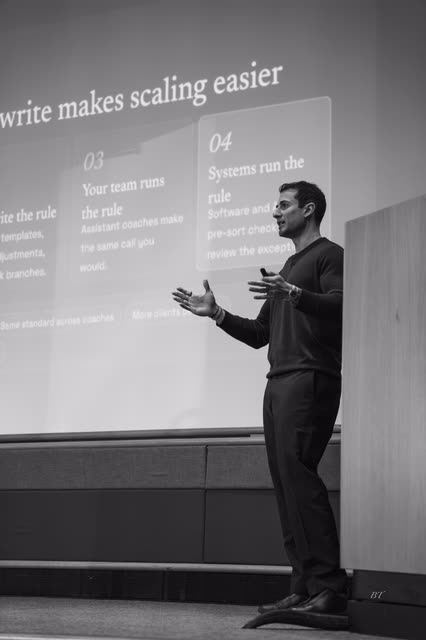 Black and white shot of a speaker presenting a systems slide