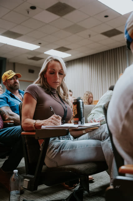 Attendee taking notes in her seat, coaches in yellow COACH hats behind her