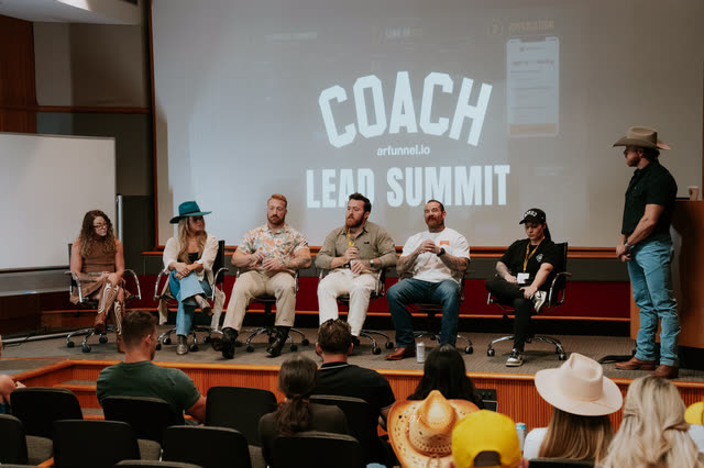 Panel of coaches seated on stage under the COACH Lead Summit screen, room watching