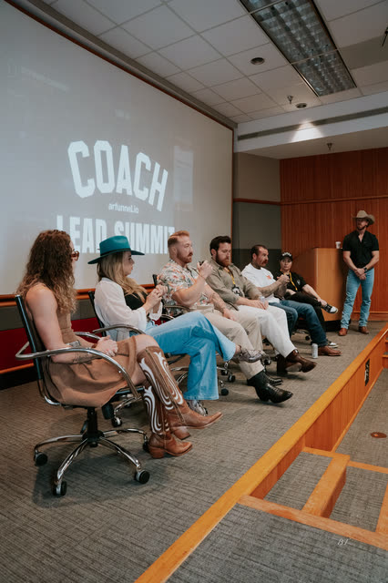 Row of panelists seated on stage under the COACH screen