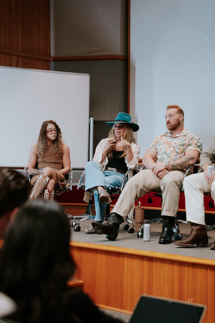 Panelists in cowboy hats and boots seated on stage, seen from the audience
