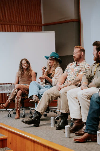 Panelist in a teal hat speaking into a microphone beside fellow coaches