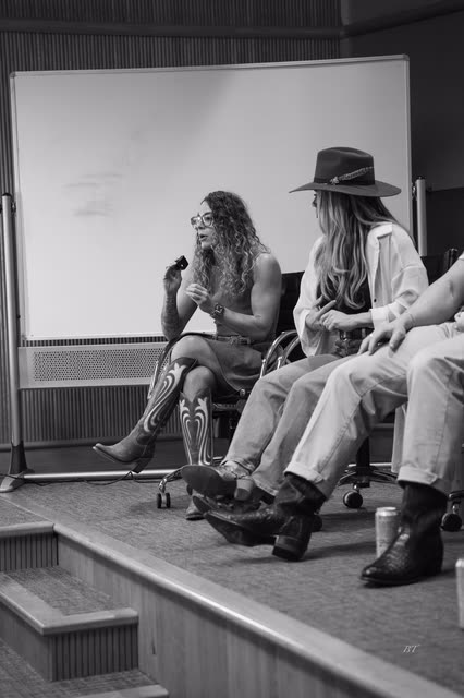 Black and white shot of a panelist speaking, boots and hats in frame