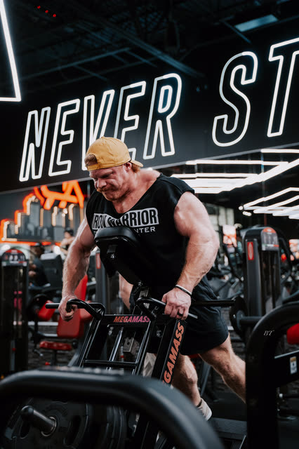 Coach in a COACH cap pulling a heavy T-bar row under the Never Stop neon
