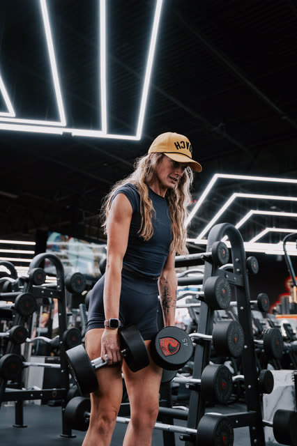 Coach in a COACH cap standing up with heavy dumbbells at the rack