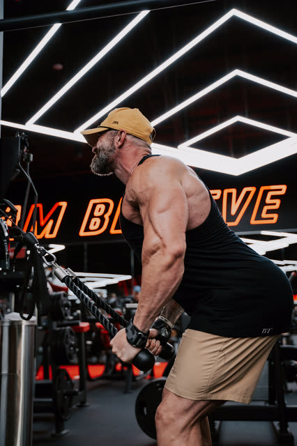 Mike Crowson leaning into a cable row under the Believe neon