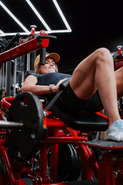 Low angle of a coach in a COACH cap pressing on the hip thrust machine