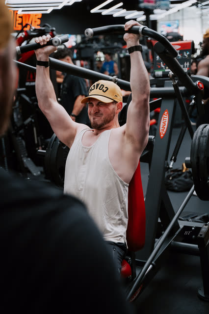 Coach in a white tank and COACH cap locking out a shoulder press
