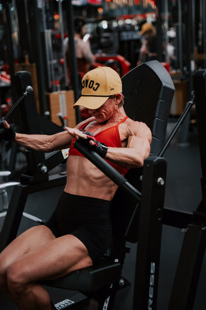 Coach in a red sports bra and COACH cap pushing through a chest press