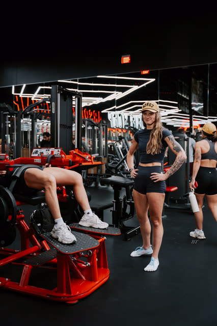 Coach in a COACH cap watching a partner on the hip thrust machine