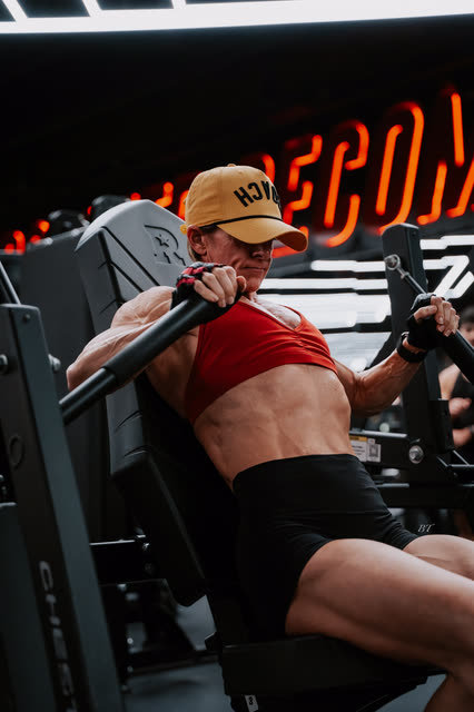 Coach in a red sports bra and COACH cap on the chest press under the Recomp neon