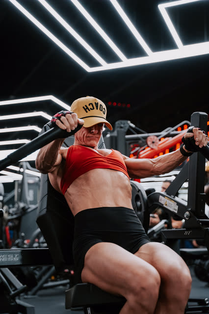 Coach in a red sports bra and COACH cap driving through a chest press