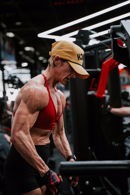 Coach in a red sports bra and COACH cap leaning into a machine row