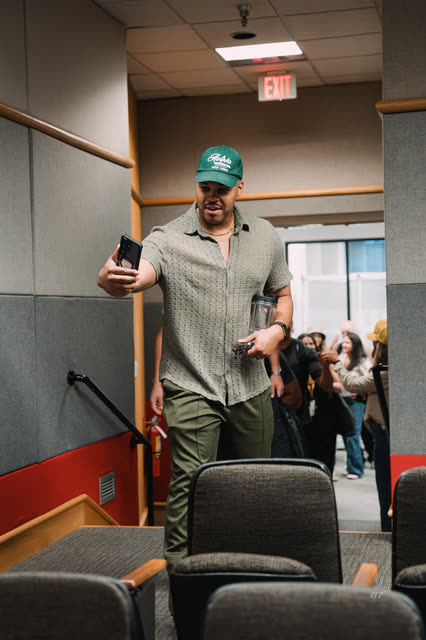 Coach in a green cap taking a selfie as he walks into the hall