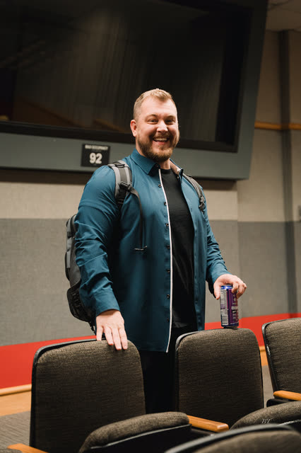 Coach in a teal shirt grinning as he finds his seat