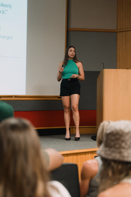 Speaker in a teal top presenting on stage beside the podium