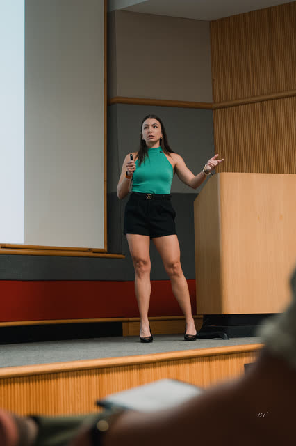 Speaker in a teal top gesturing mid-talk on stage